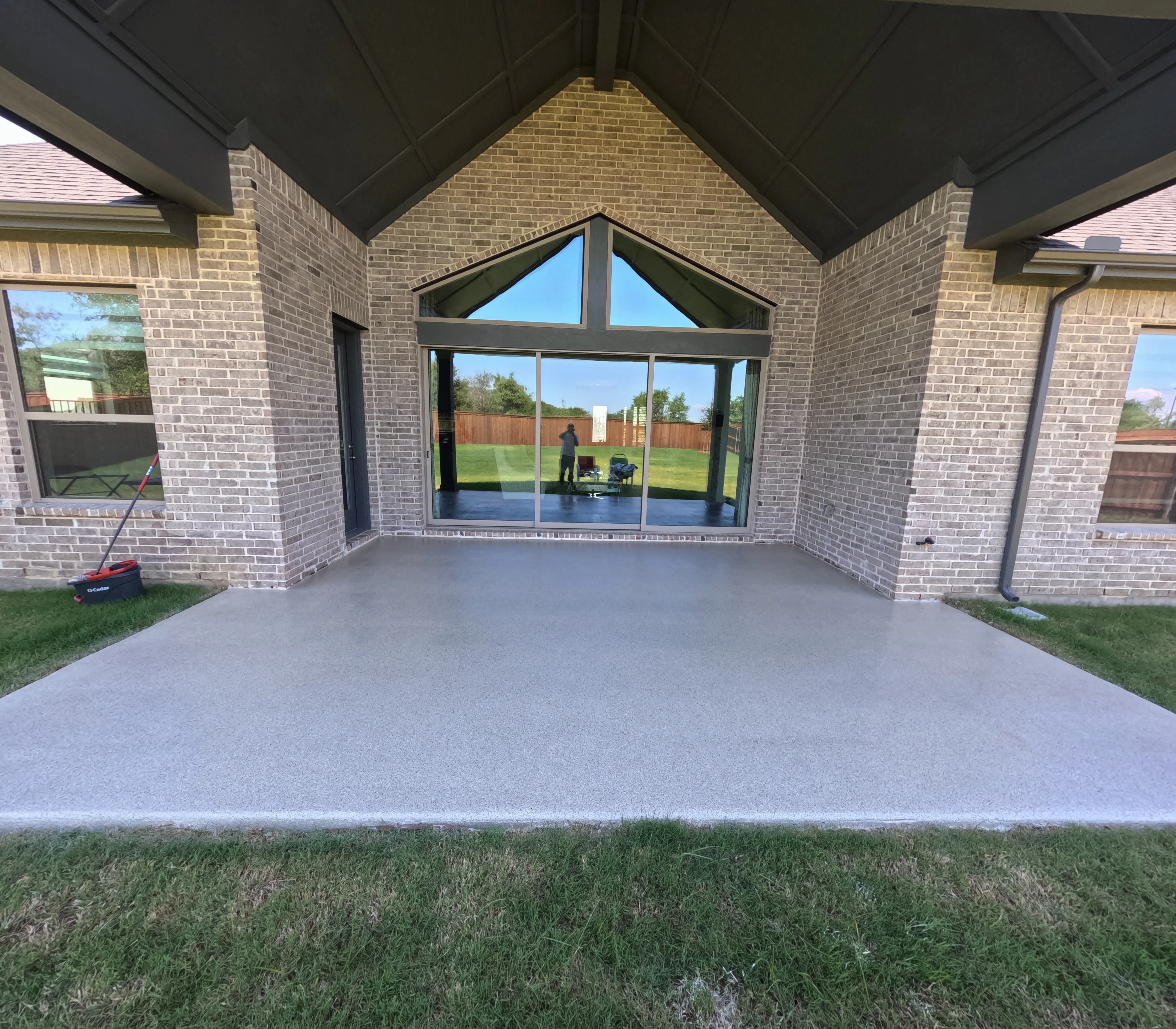 Polished concrete patio under brick pergola with large glass doors overlooking lawn