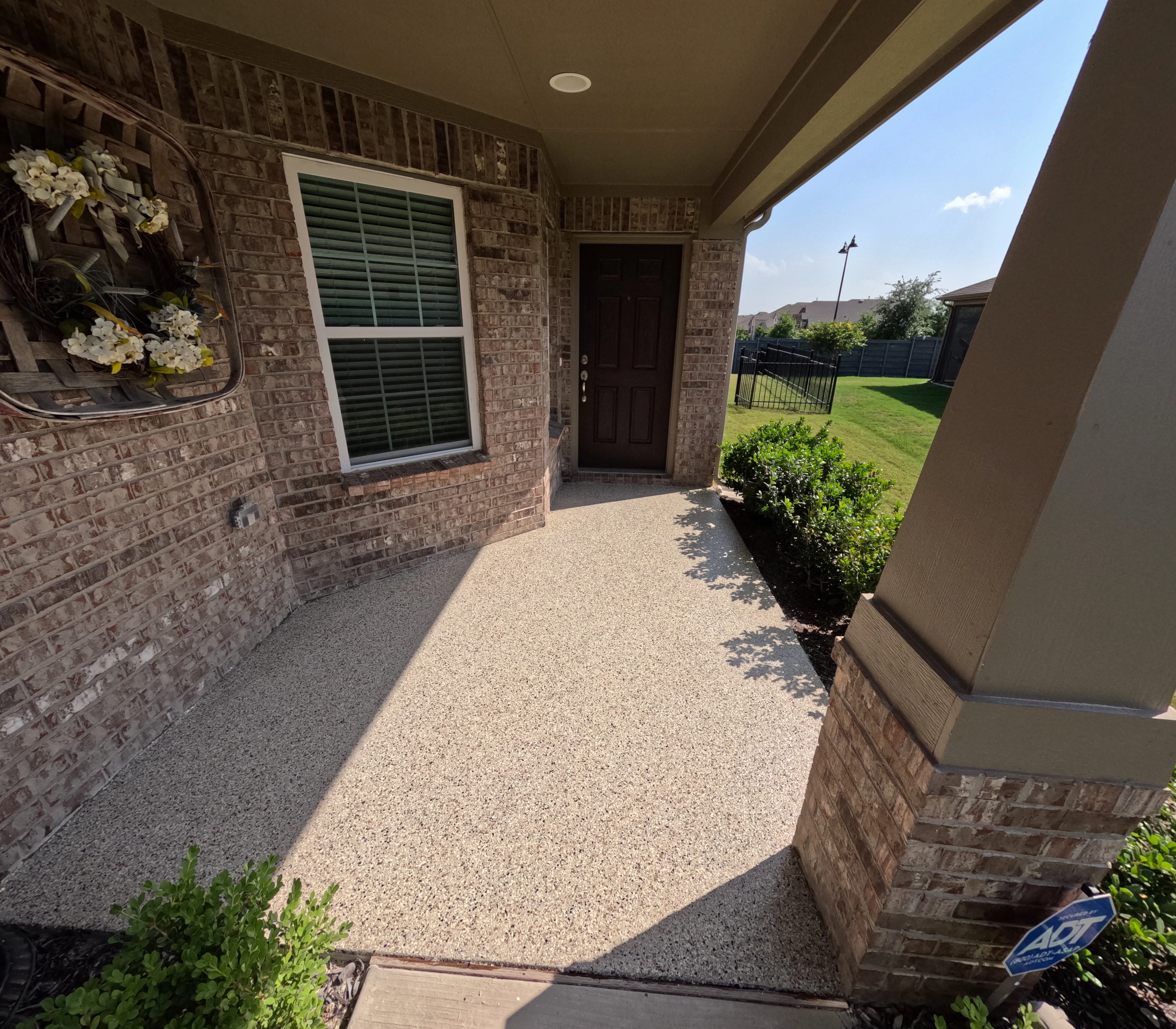 Decorative aggregate patio with tan stone finish along brick home exterior